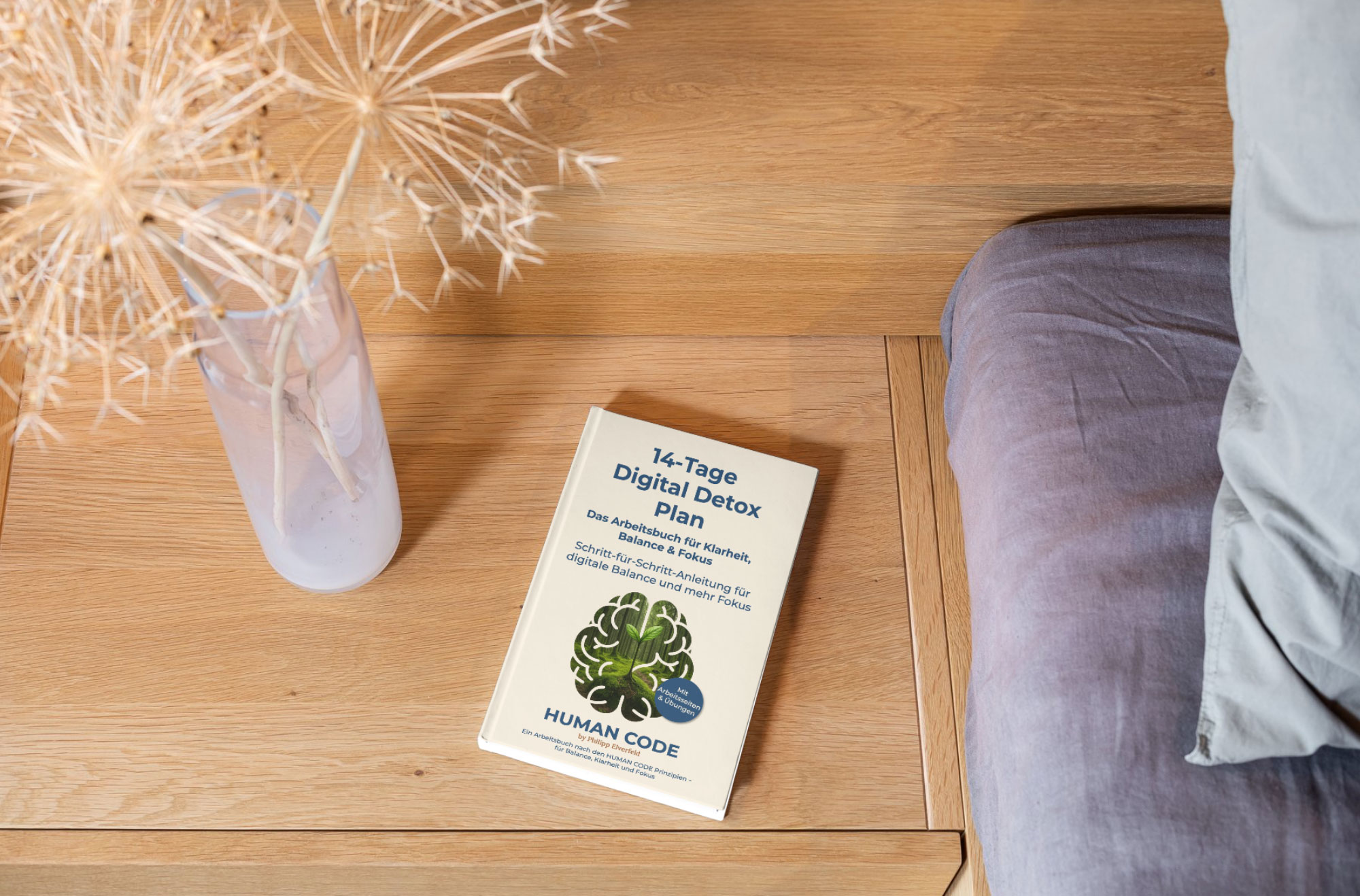 Taschenbuch „14-Tage Digital Detox Plan“ liegt auf einem Nachttisch neben einer Vase und einem Bett